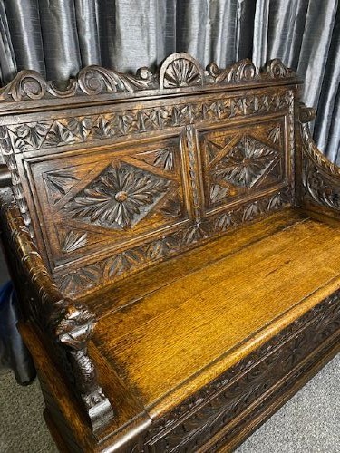 A dark carved oak storage bench featuring a high backrest with geometric floral panels and a enclosed box seat base. View II