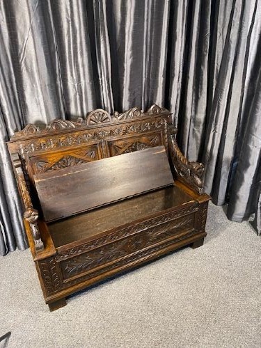 A dark carved oak storage bench featuring a high backrest with geometric floral panels and a enclosed box seat base. View VI