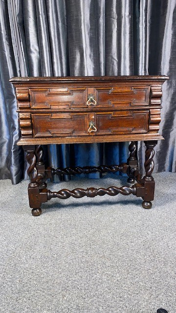 A dark oak side table featuring two drawers with geometric mouldings, brass teardrop handles, barley twist legs, and matching lower stretchers.