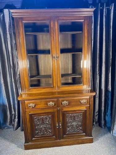 A tall Victorian walnut bookcase featuring a two-door glazed upper display section, two middle drawers with metal handles, and carved panel doors at the base.