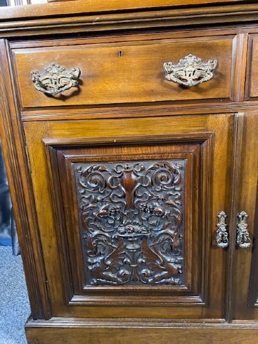 A tall Victorian walnut bookcase featuring a two-door glazed upper display section, two middle drawers with metal handles, and carved panel doors at the base. View IV