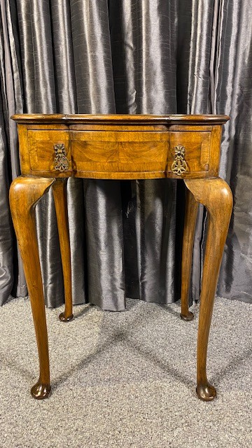 A Queen Anne style walnut occasional table featuring slender cabriole legs, pad feet, and a single drawer fitted with two ornate brass drop handles.