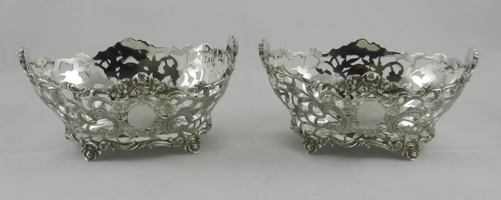 A pair of silver baskets featuring pierced openwork pattern and floral scroll accents.