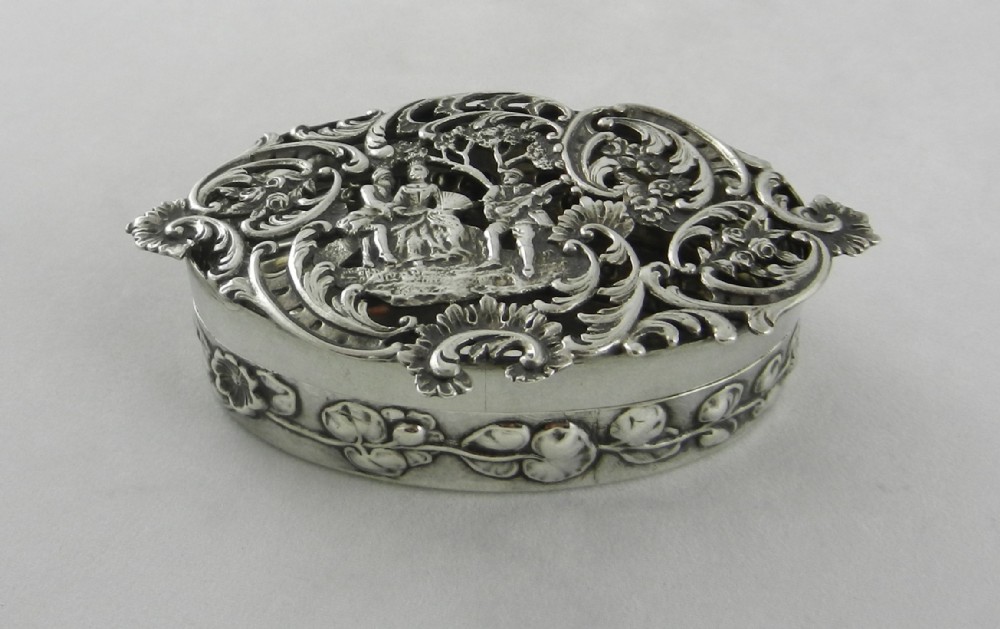 An oval silver pot pourri box with an intricately pierced lid featuring a pastoral scene framed by rococo scrollwork.