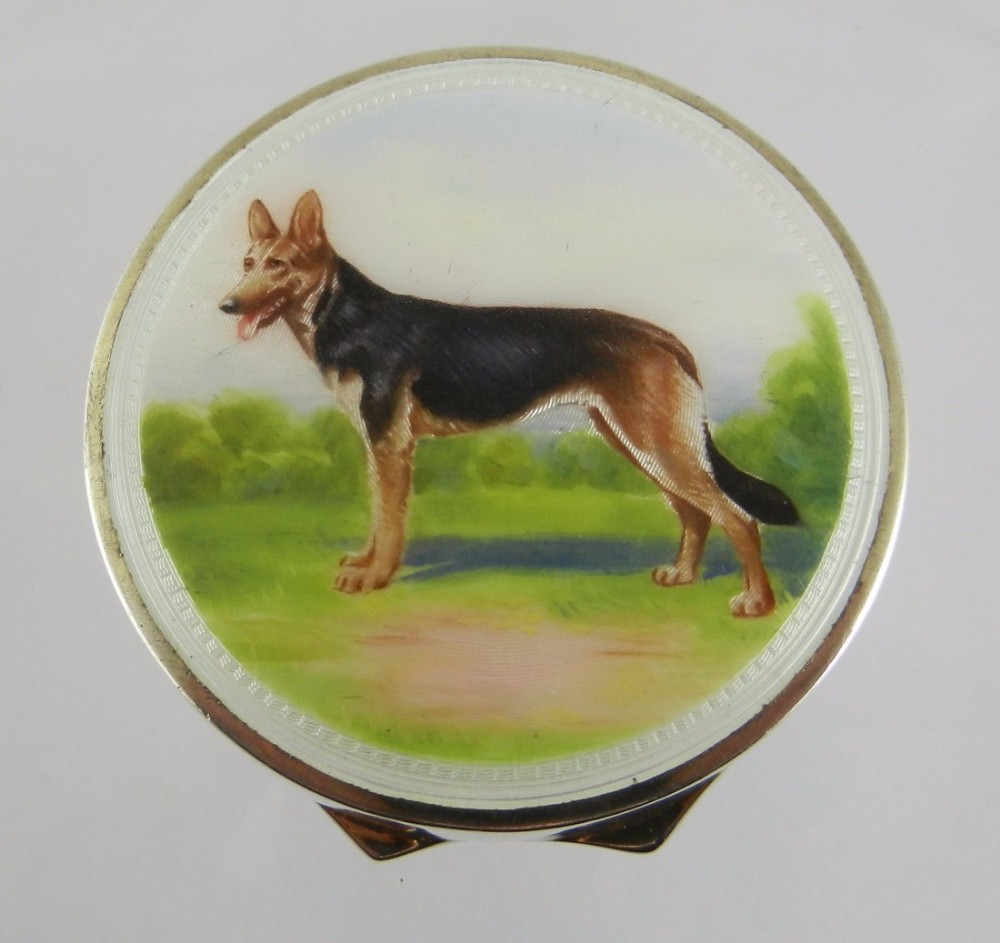 A circular silver-gilt compact featuring a white guilloche enamel lid decorated with a hand-painted German Shepherd dog in a grassy landscape.