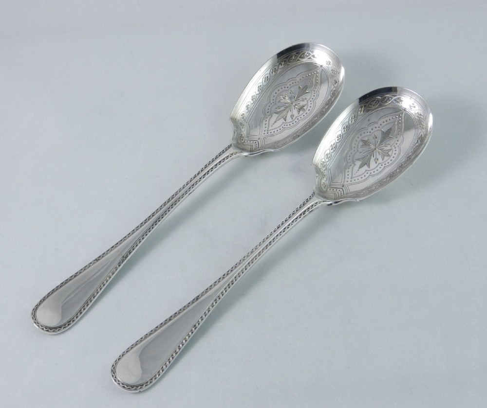 A pair of antique silver-plated fruit spoons featuring bright-cut engraved starburst patterns on the bowls and patterned borders on the handles.