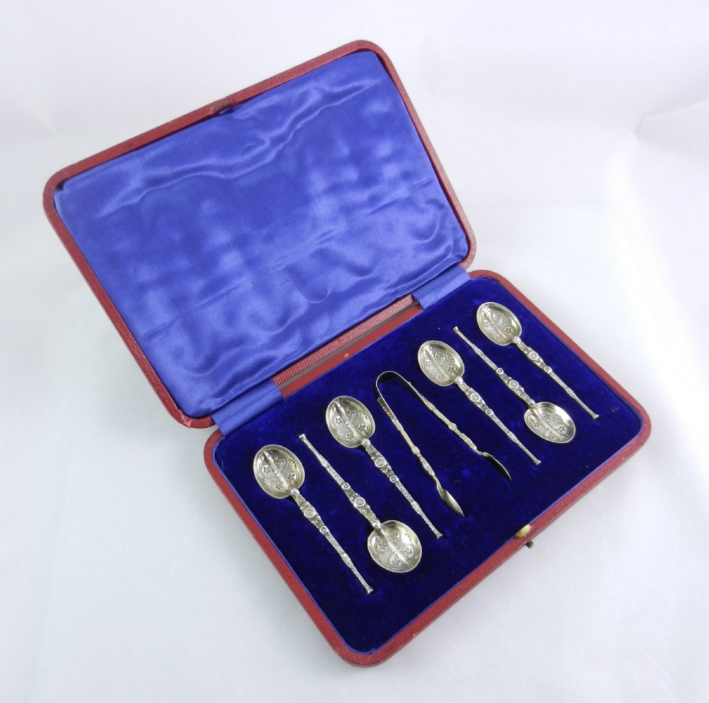 An open red presentation case lined with blue silk and velvet holding six silver-gilt teaspoons and a pair of matching sugar tongs.
