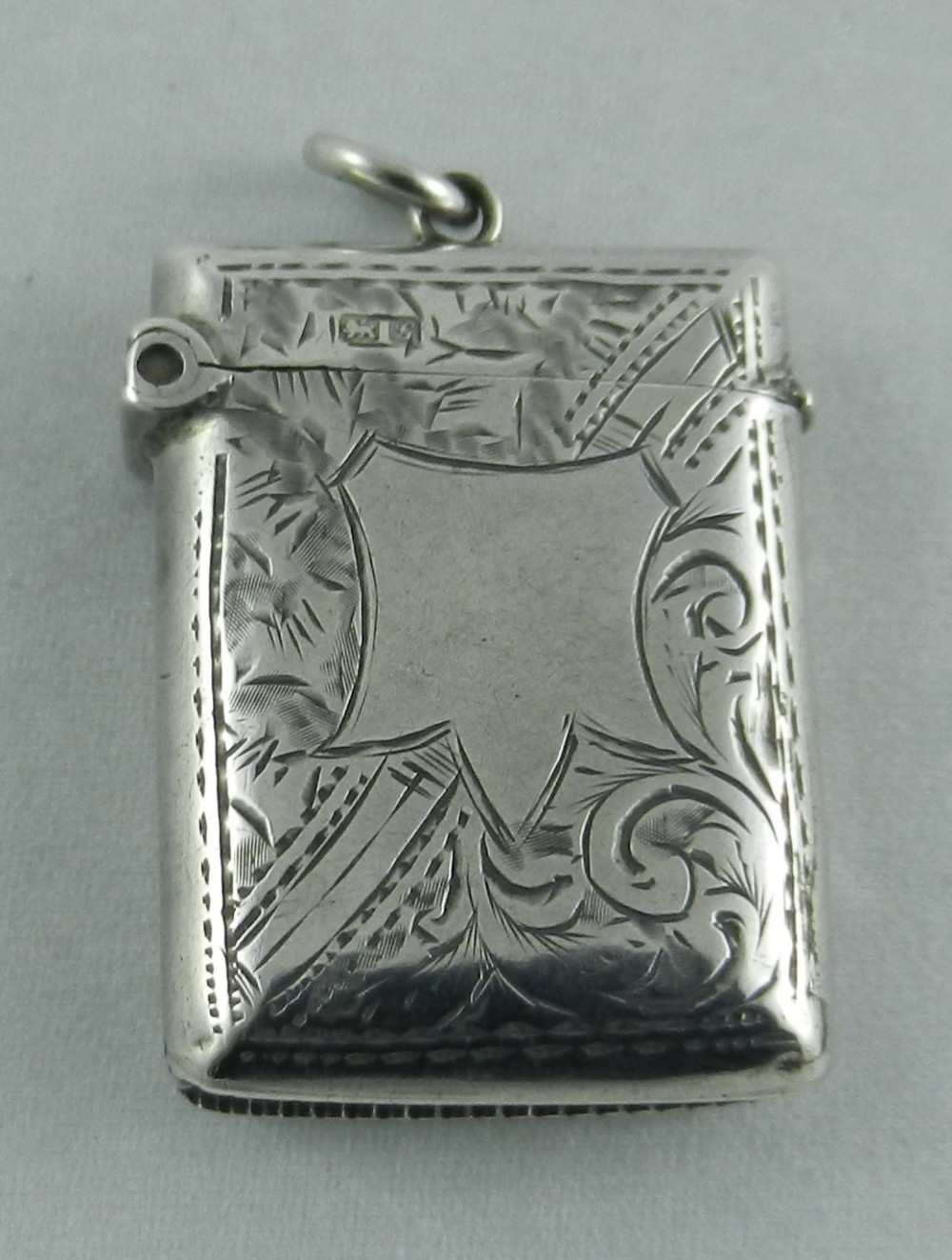 An antique engraved sterling silver vesta case featuring foliate scrollwork, an unengraved shield cartouche, visible hallmarks, and a top ring.