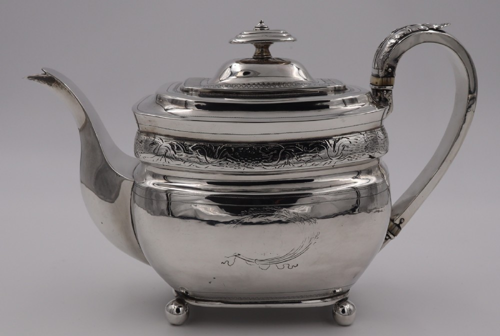 An antique sterling silver teapot with engraved foliate motifs, an oblong body, ball feet, and a hinged lid. View II