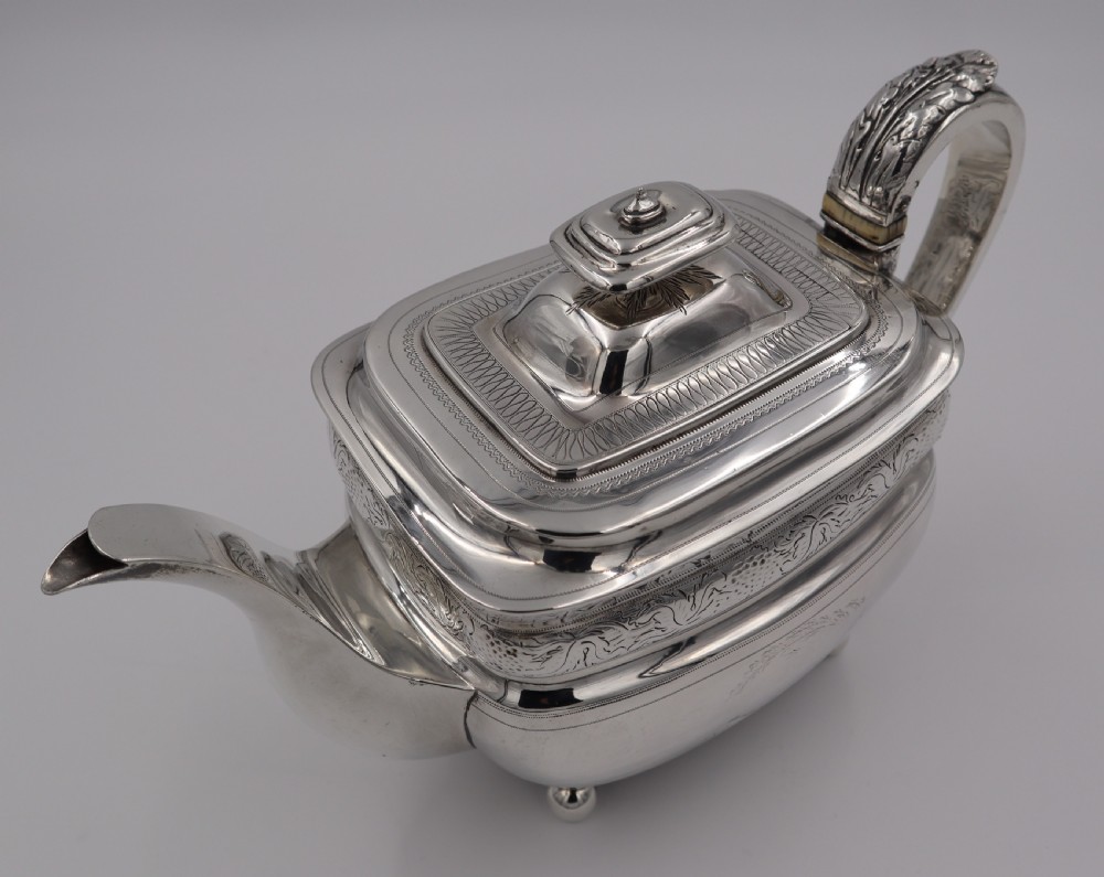 An antique sterling silver teapot with engraved foliate motifs, an oblong body, ball feet, and a hinged lid. View III
