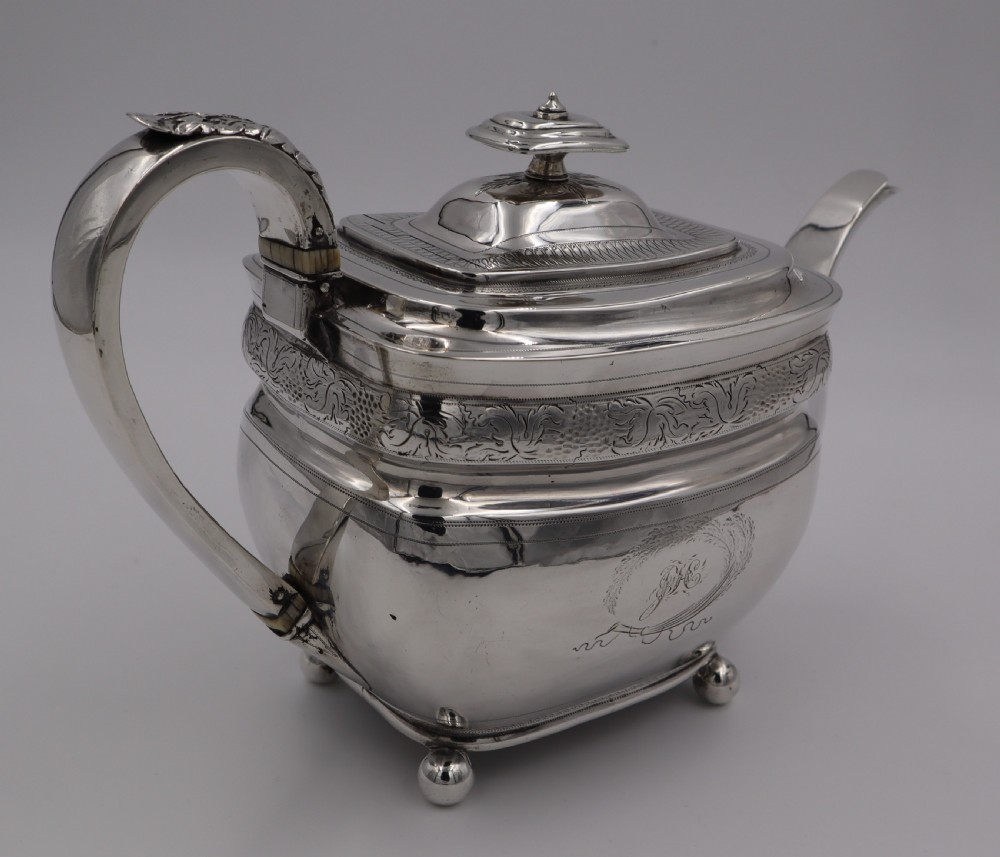 An antique sterling silver teapot with engraved foliate motifs, an oblong body, ball feet, and a hinged lid. View V