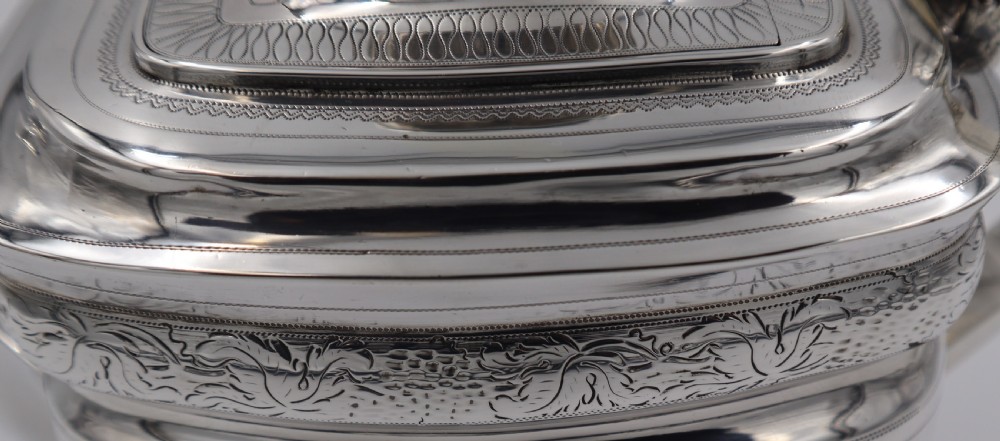 An antique sterling silver teapot with engraved foliate motifs, an oblong body, ball feet, and a hinged lid. View VI