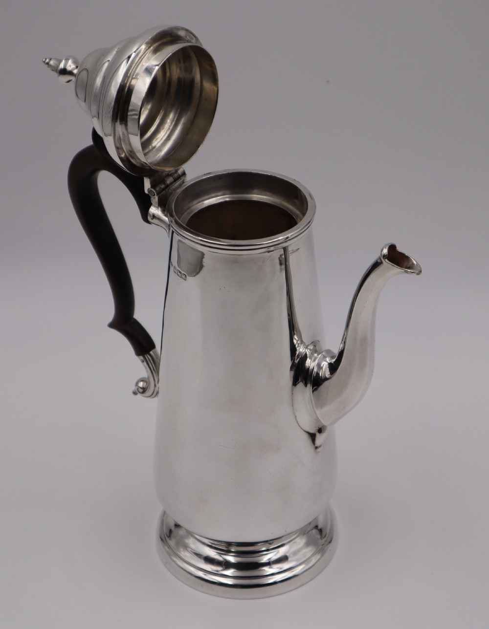 A tall silver coffee pot featuring a tapered body, stepped domed lid with finial, a curved goose-neck spout, visible hallmarks, and a dark carved wooden handle. View III