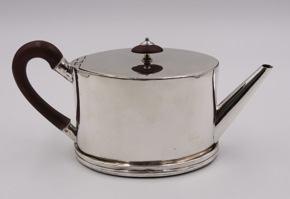 A cylindrical silver teapot with a dark wood handle and finial resting on a matching fitted silver stand.