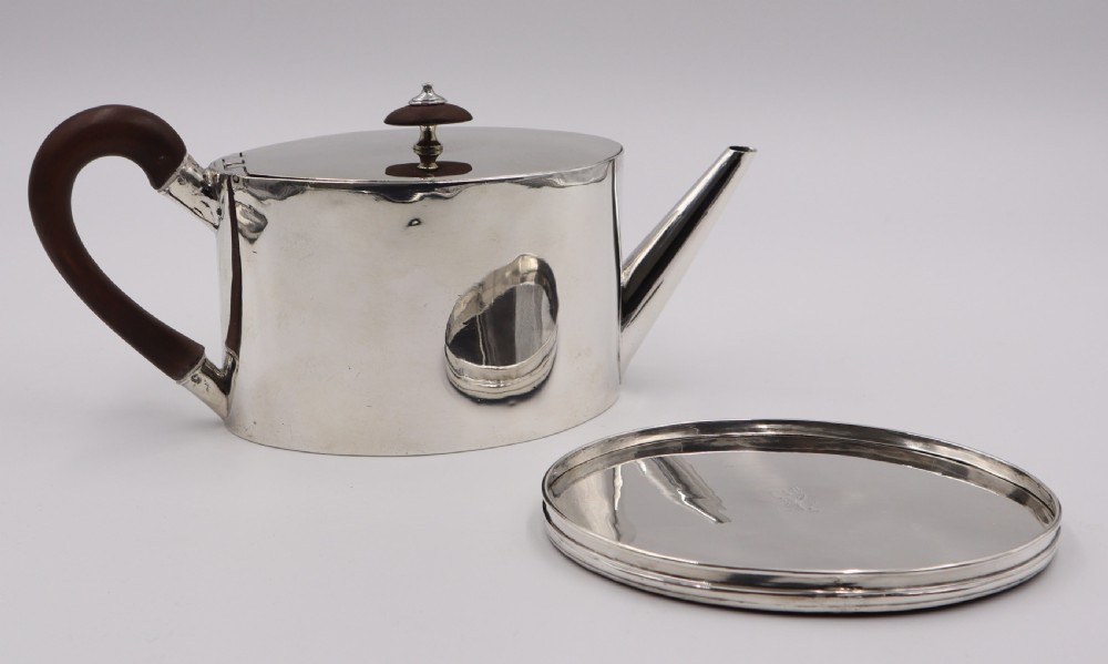 A cylindrical silver teapot with a dark wood handle and finial resting on a matching fitted silver stand. View II
