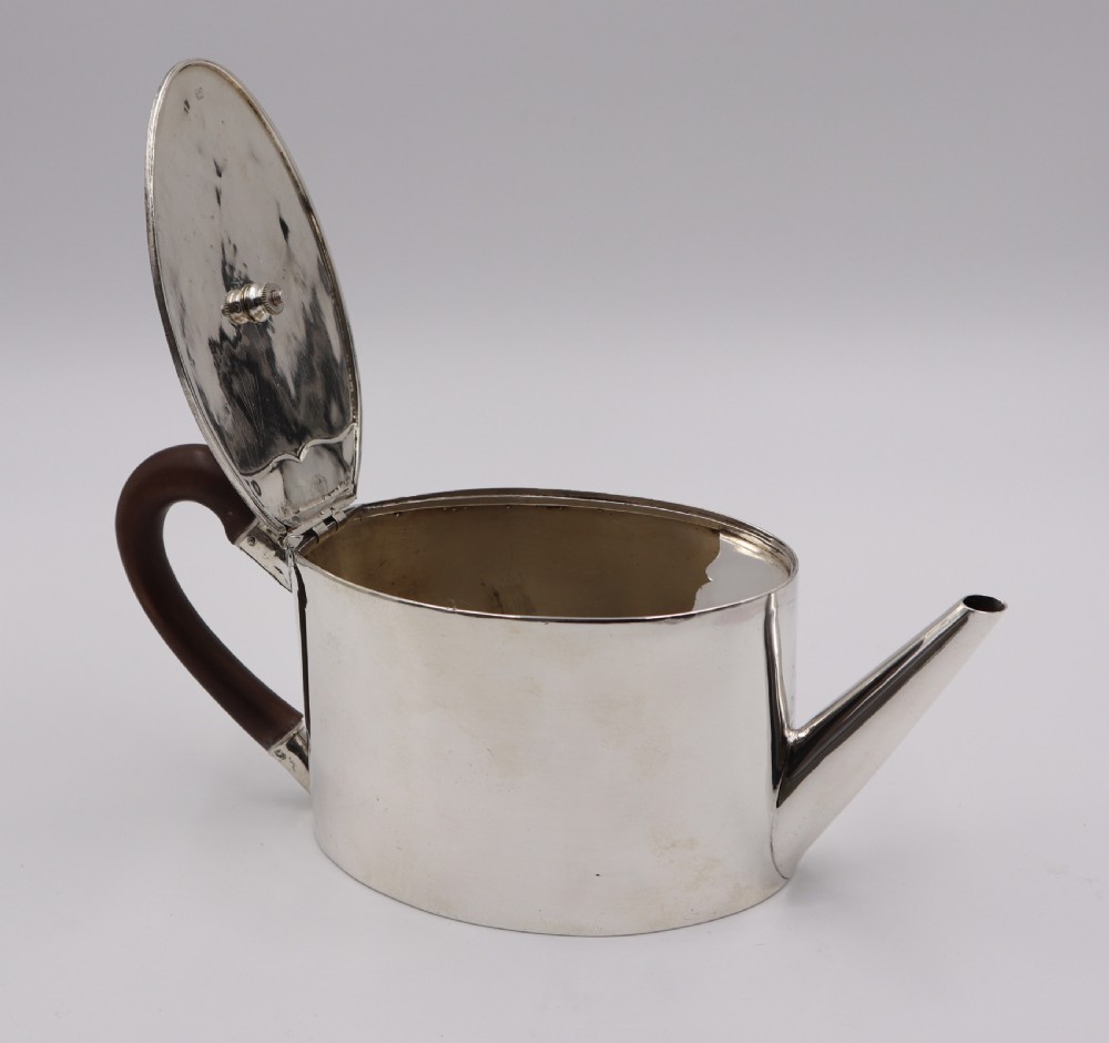 A cylindrical silver teapot with a dark wood handle and finial resting on a matching fitted silver stand. View III