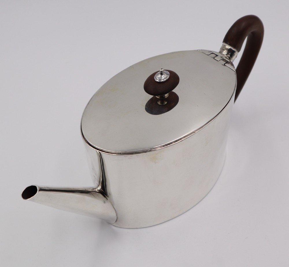 A cylindrical silver teapot with a dark wood handle and finial resting on a matching fitted silver stand. View IV