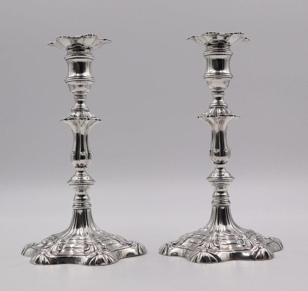 A pair of polished silver candlesticks featuring knopped stems, scalloped nozzles, and moulded shell-shaped bases with visible assay hallmarks.