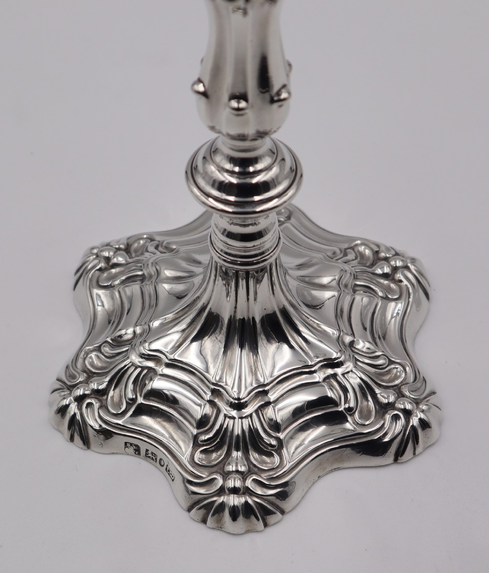 A pair of polished silver candlesticks featuring knopped stems, scalloped nozzles, and moulded shell-shaped bases with visible assay hallmarks. View V