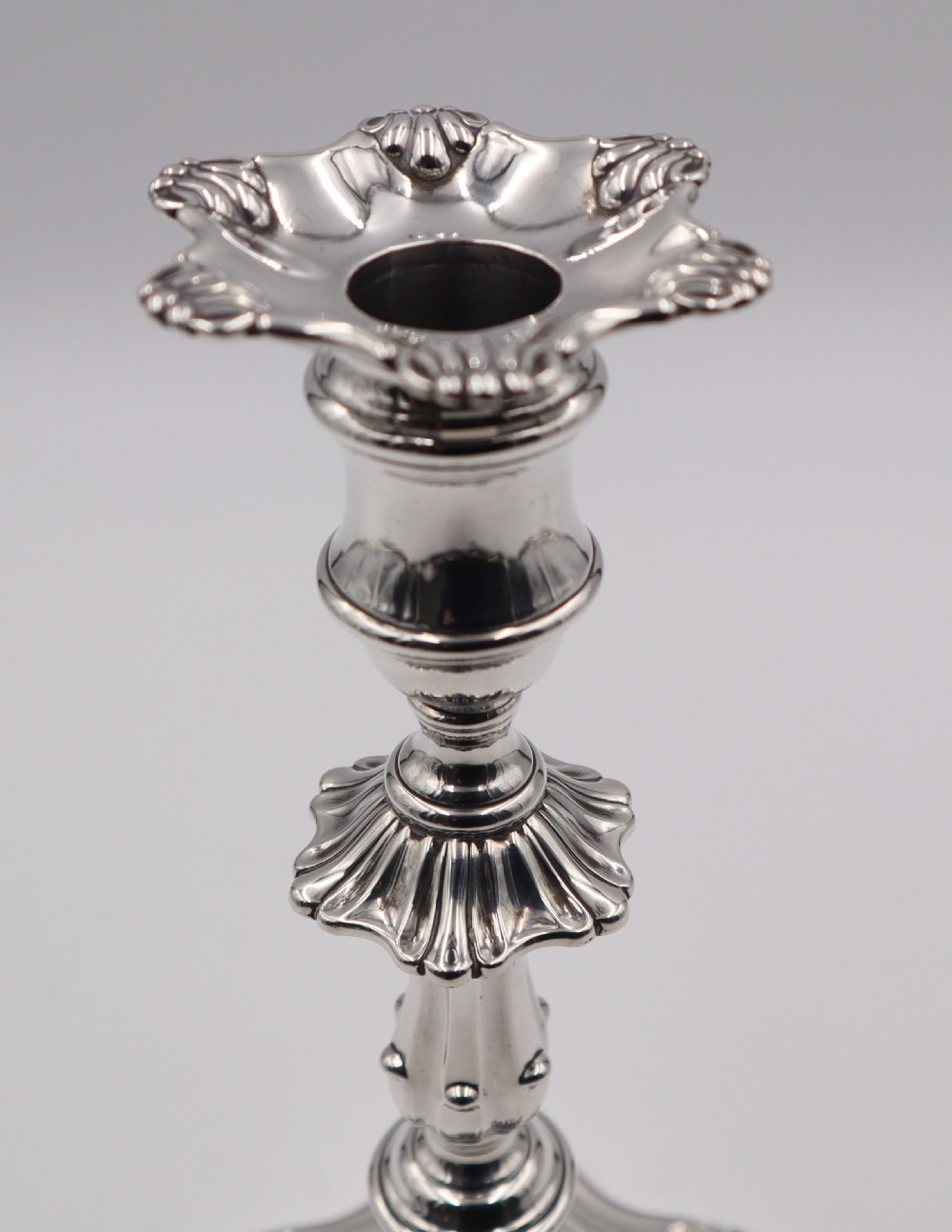 A pair of polished silver candlesticks featuring knopped stems, scalloped nozzles, and moulded shell-shaped bases with visible assay hallmarks. View VI