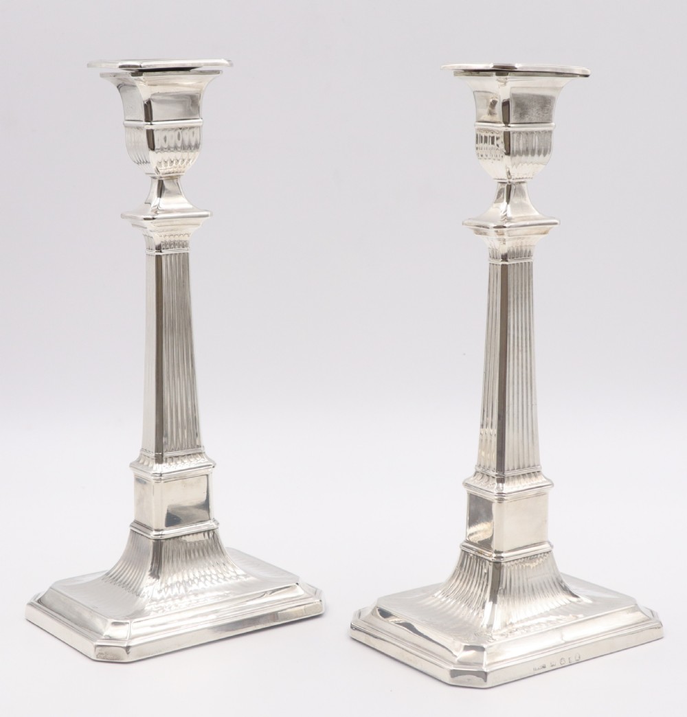 A pair of antique sterling silver candlesticks featuring fluted column shafts and square stepped bases.