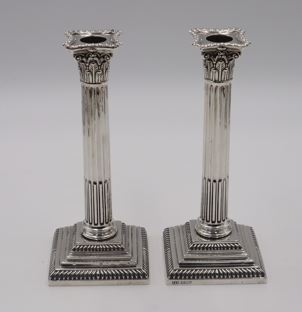 A pair of hallmarked silver Corinthian column candlesticks featuring fluted shafts and stepped square bases.