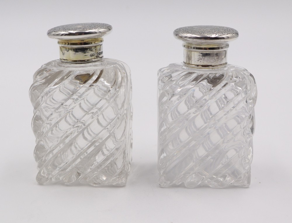 A pair of clear cut-glass perfume bottles featuring diagonal swirl moulding and engraved silver caps.