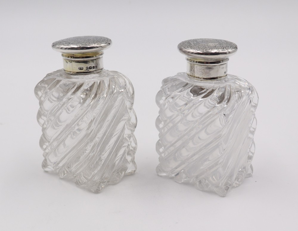 A pair of clear cut-glass perfume bottles featuring diagonal swirl moulding and engraved silver caps. View II