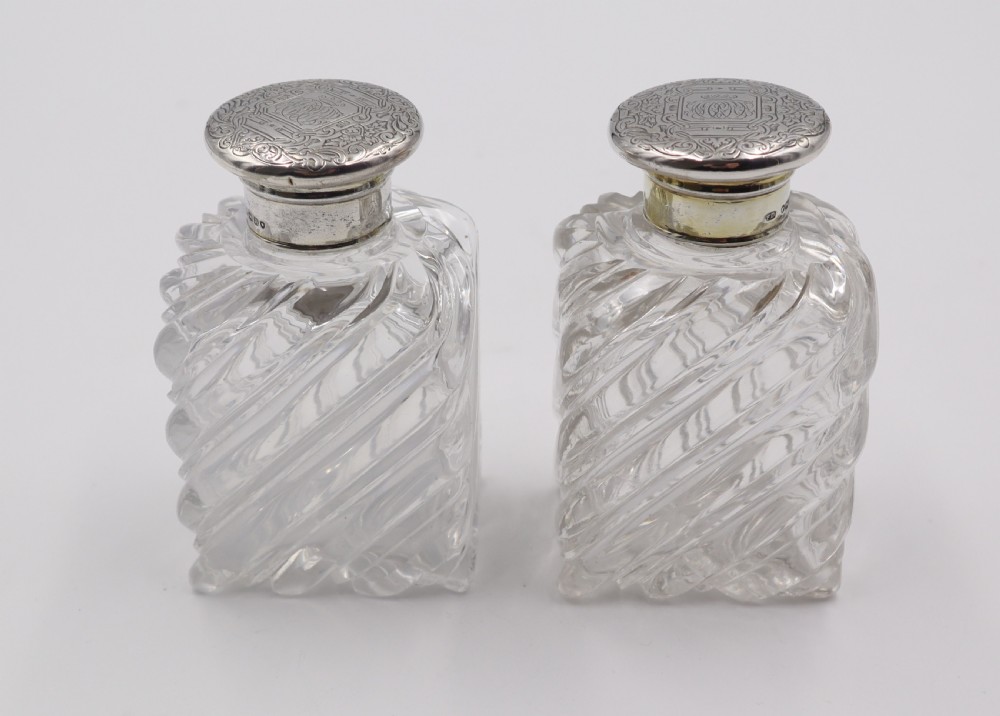 A pair of clear cut-glass perfume bottles featuring diagonal swirl moulding and engraved silver caps. View IV