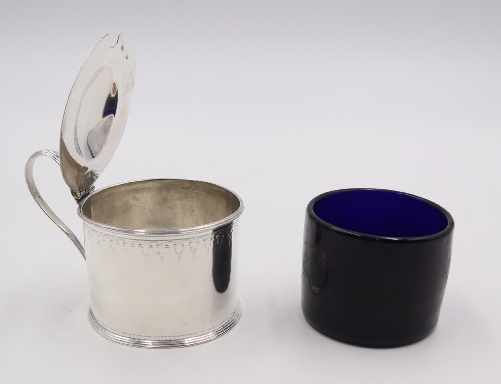 A cylindrical sterling silver mustard pot featuring a domed hinged lid with a thumbpiece, a loop handle, and engraved bright-cut detailing around the upper rim. View IV