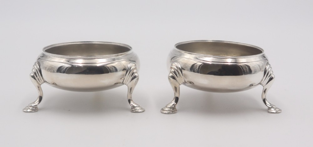 A pair of circular silver open salt cellars, each elevated on three cabriole legs with decorative knees and pad feet.