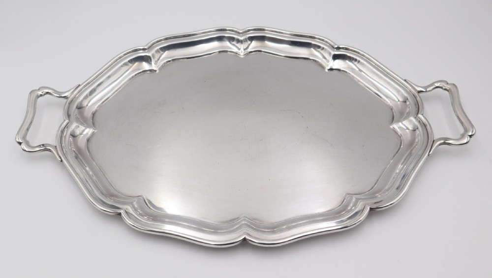 An oval silver-plated serving tray featuring a scalloped molded rim, twin integrated side handles, and a polished metallic surface.