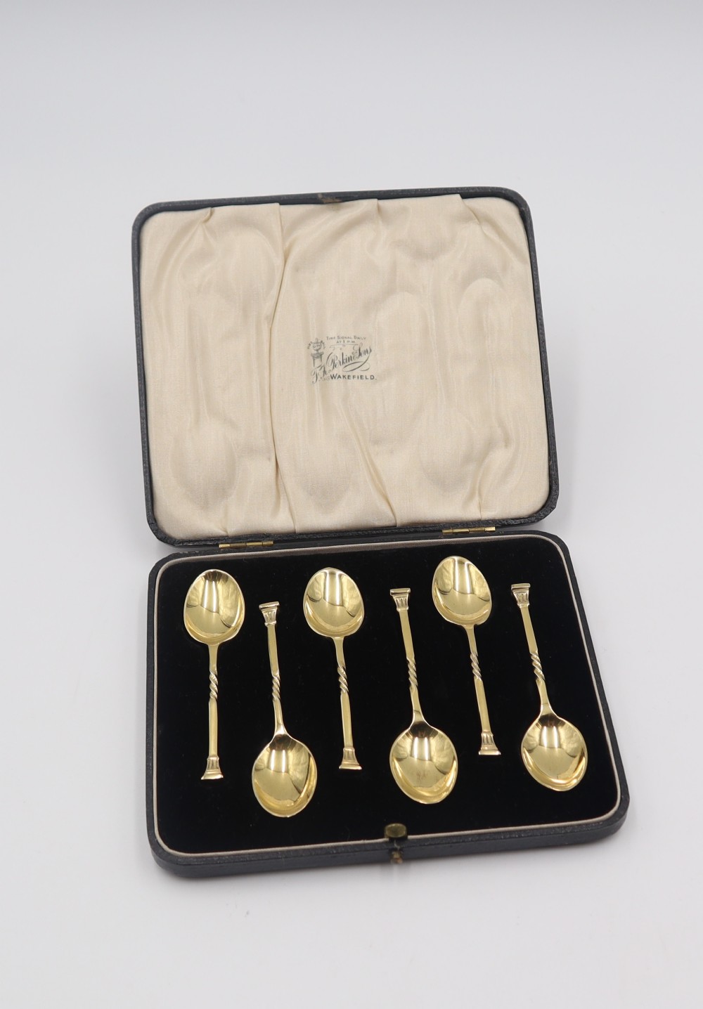 A set of six silver-gilt spoons with twisted stems displayed inside a fitted black presentation case lined with cream silk and black velvet.