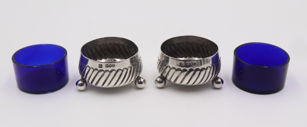 A pair of circular silver salt cellars featuring spiral-fluted bodies, three small ball feet, and removable cobalt blue glass liners. View IV