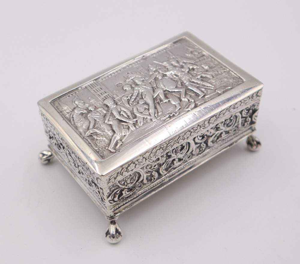 A rectangular silver trinket box featuring an embossed relief scene of Napoleon on the lid, ornate filigree side panels, and small raised ball feet. View V