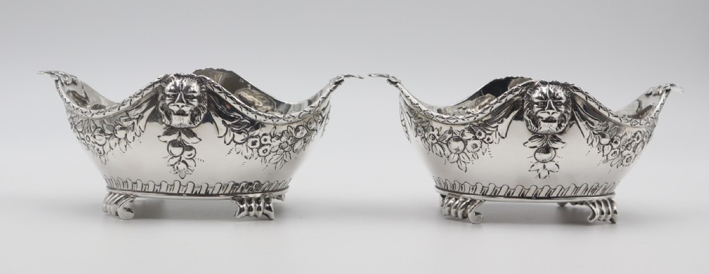 A pair of ornate antique silver bowls featuring embossed lion head masks, floral swags, gadrooned bases, and scroll feet.