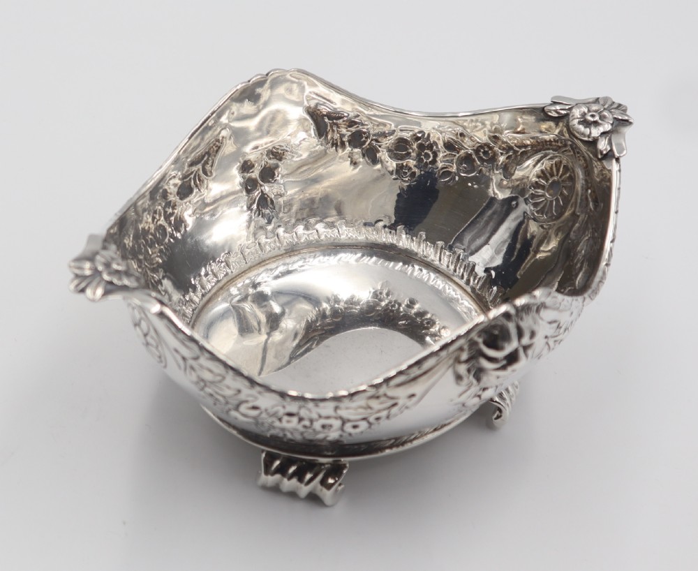 A pair of ornate antique silver bowls featuring embossed lion head masks, floral swags, gadrooned bases, and scroll feet. View V