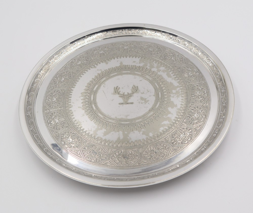 A circular silverplated salver featuring intricate engraved circular patterns and a central crest depicting a stags head.