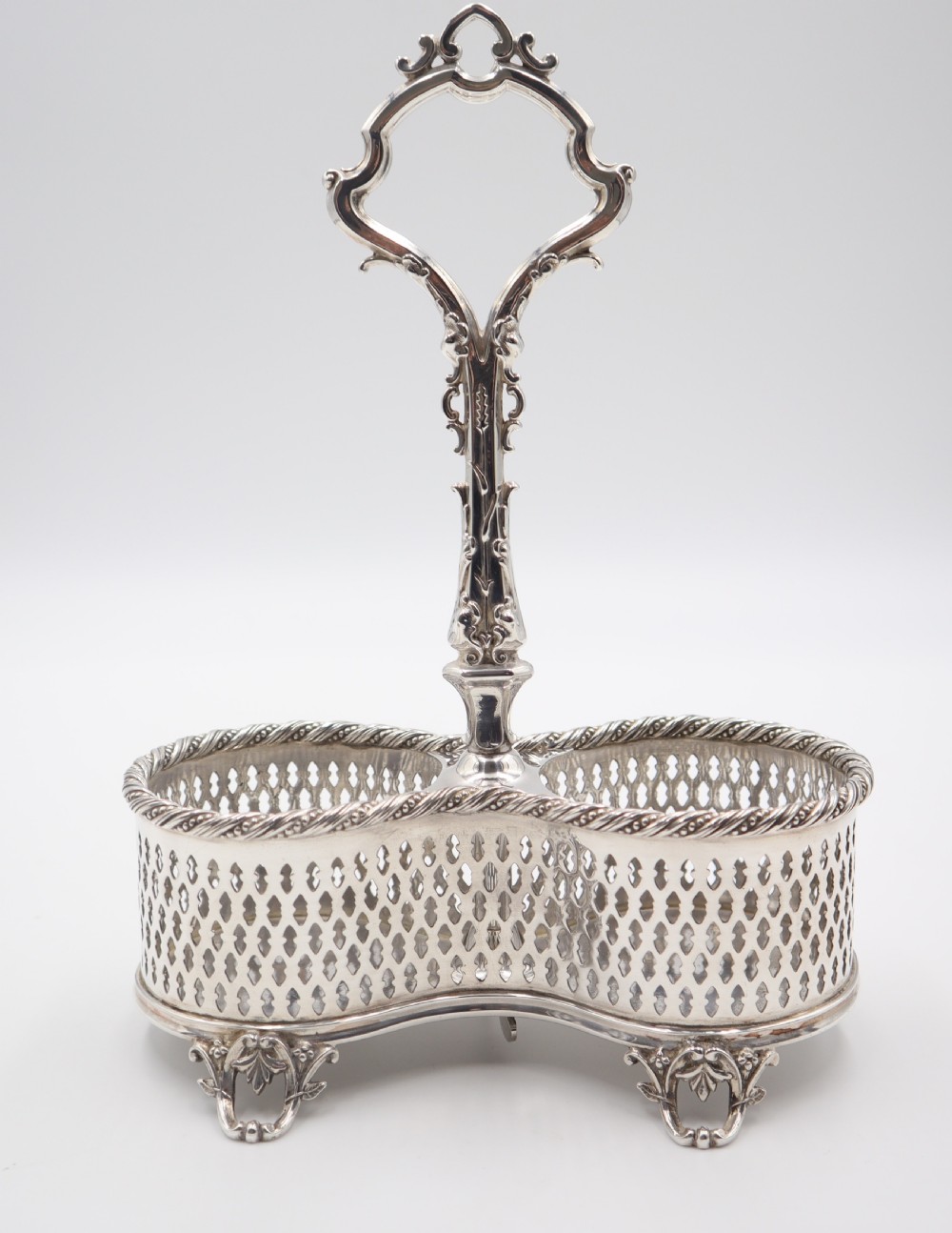 An antique silver-plated liqueur stand featuring a pierced lattice gallery, decorative central handle, and scroll feet, holding two cut-glass decanters with stoppers. View IV
