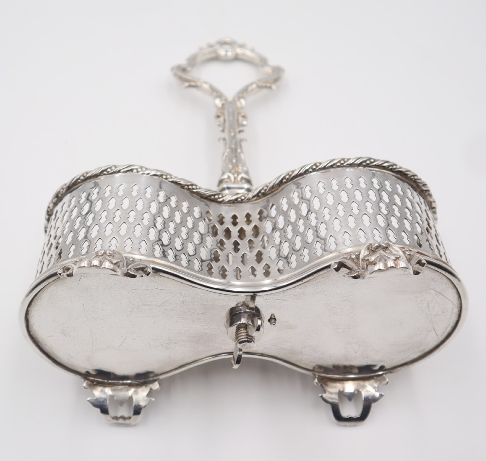 An antique silver-plated liqueur stand featuring a pierced lattice gallery, decorative central handle, and scroll feet, holding two cut-glass decanters with stoppers. View V