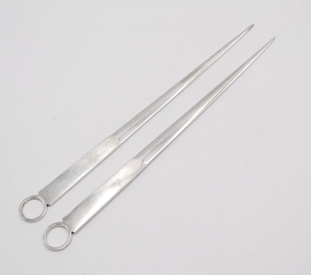 A pair of antique silver-plated meat skewers featuring flat tapered blades and circular ring finials. View II