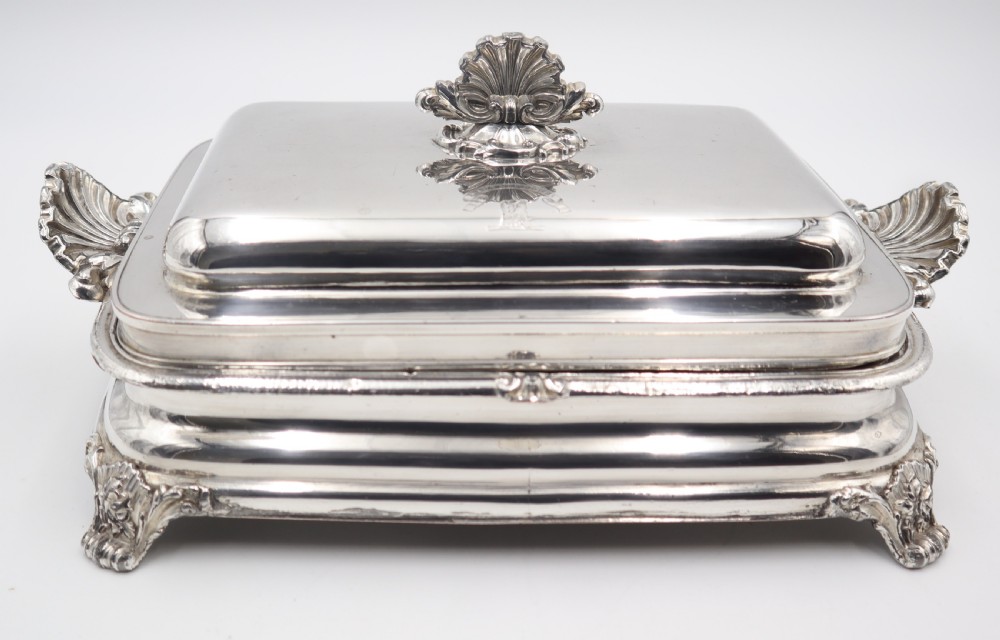 A rectangular silver-plated warming entree dish featuring shell-form handles, a domed lid with a shell finial, and a raised pedestal base.
