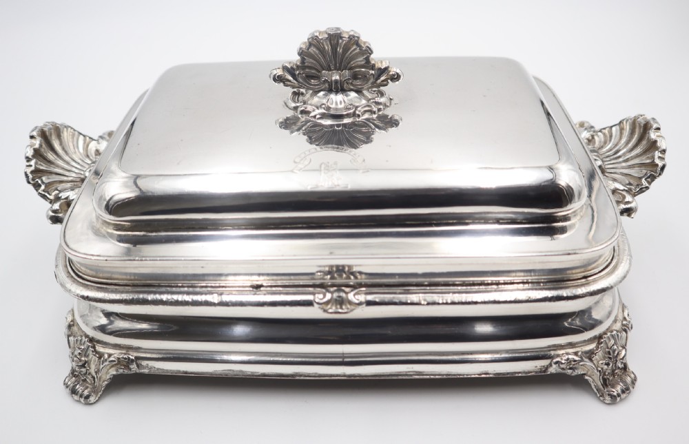 A rectangular silver-plated warming entree dish featuring shell-form handles, a domed lid with a shell finial, and a raised pedestal base. View VI