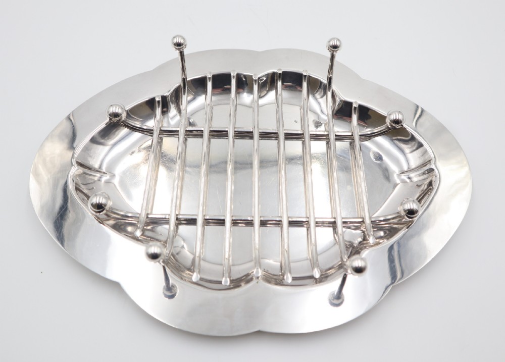 An oval silver-plated dish featuring a scalloped rim and a removable central wire rack supported by small spherical feet.
