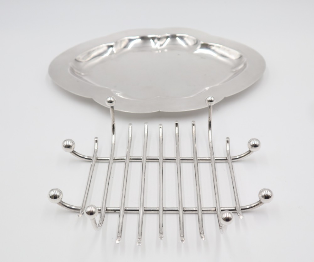 An oval silver-plated dish featuring a scalloped rim and a removable central wire rack supported by small spherical feet. View II