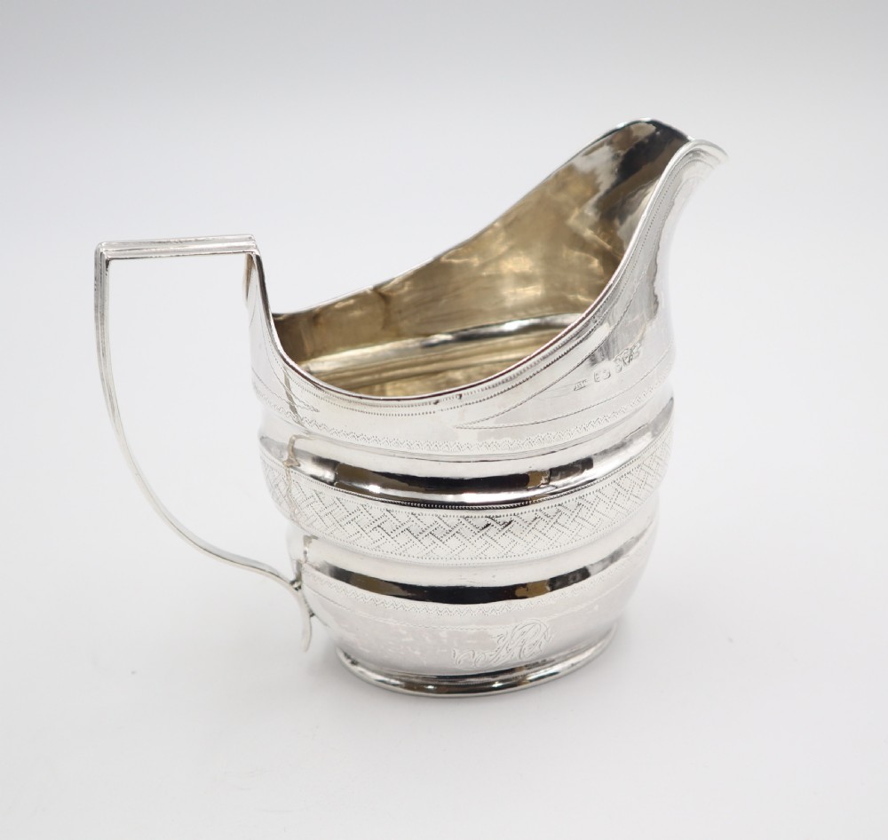 An antique sterling silver cream jug featuring geometric engraved banding, reeded body contours, an angular strap handle, and a polished metallic surface. View II