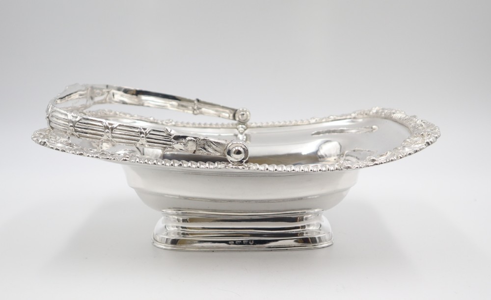 An antique rectangular silver-plated cake basket featuring an overhead swing handle and gadrooned rim with shell corner motifs. View IV