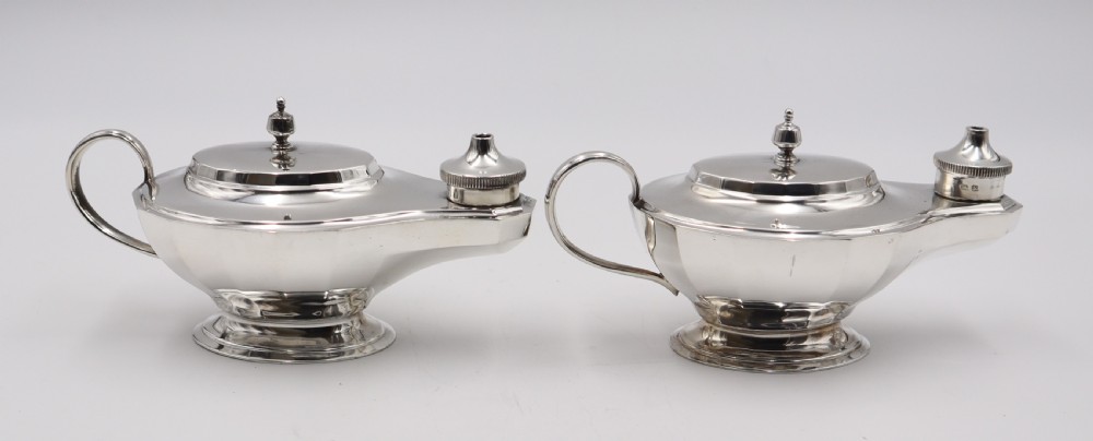 A pair of polished silver table lighters designed in the traditional shape of classical oil lamps with curved loop handles and pedestal bases.