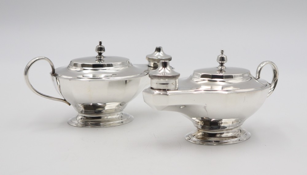 A pair of polished silver table lighters designed in the traditional shape of classical oil lamps with curved loop handles and pedestal bases. View II