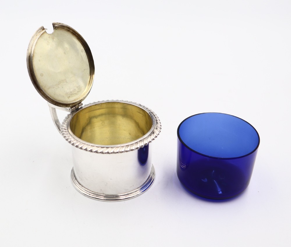 A cylindrical sterling silver mustard pot featuring a flat hinged lid, shell thumbpiece, rope twist trim, and an angular handle. View VI
